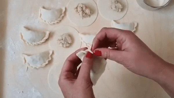 Hands shaping pierogi dumplings on floured countertop in kitchen