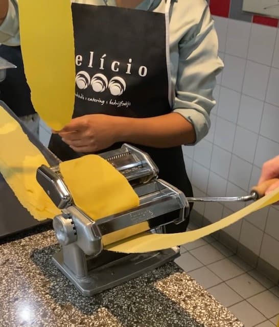 Fresh pasta rolled through manual pasta maker in tiled kitchen