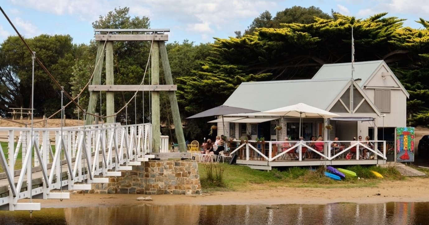 Historic riverside picnic spot with white footbridge and boathouse