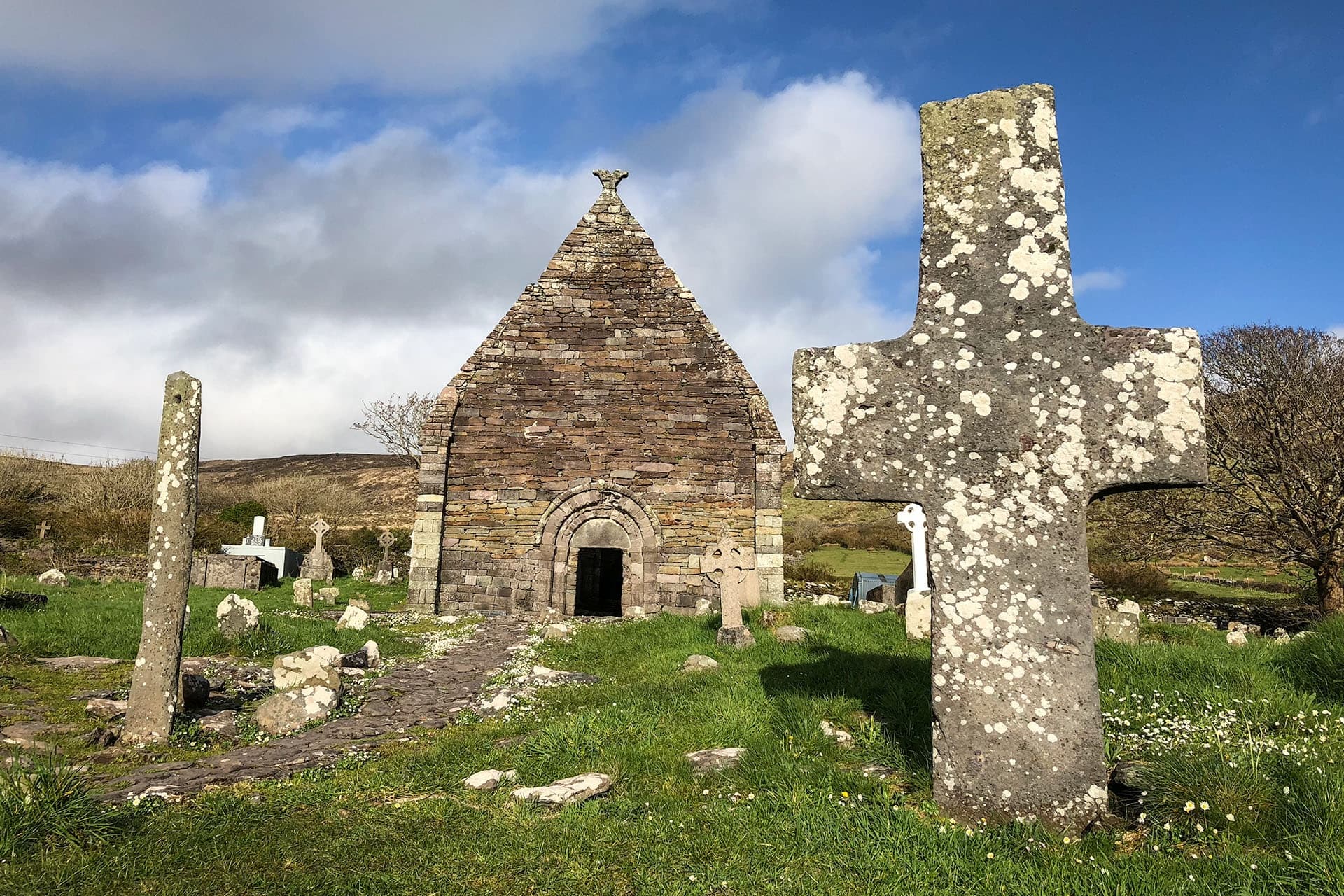 Ancient stone cross and chapel ruins on green Irish coastal landscape