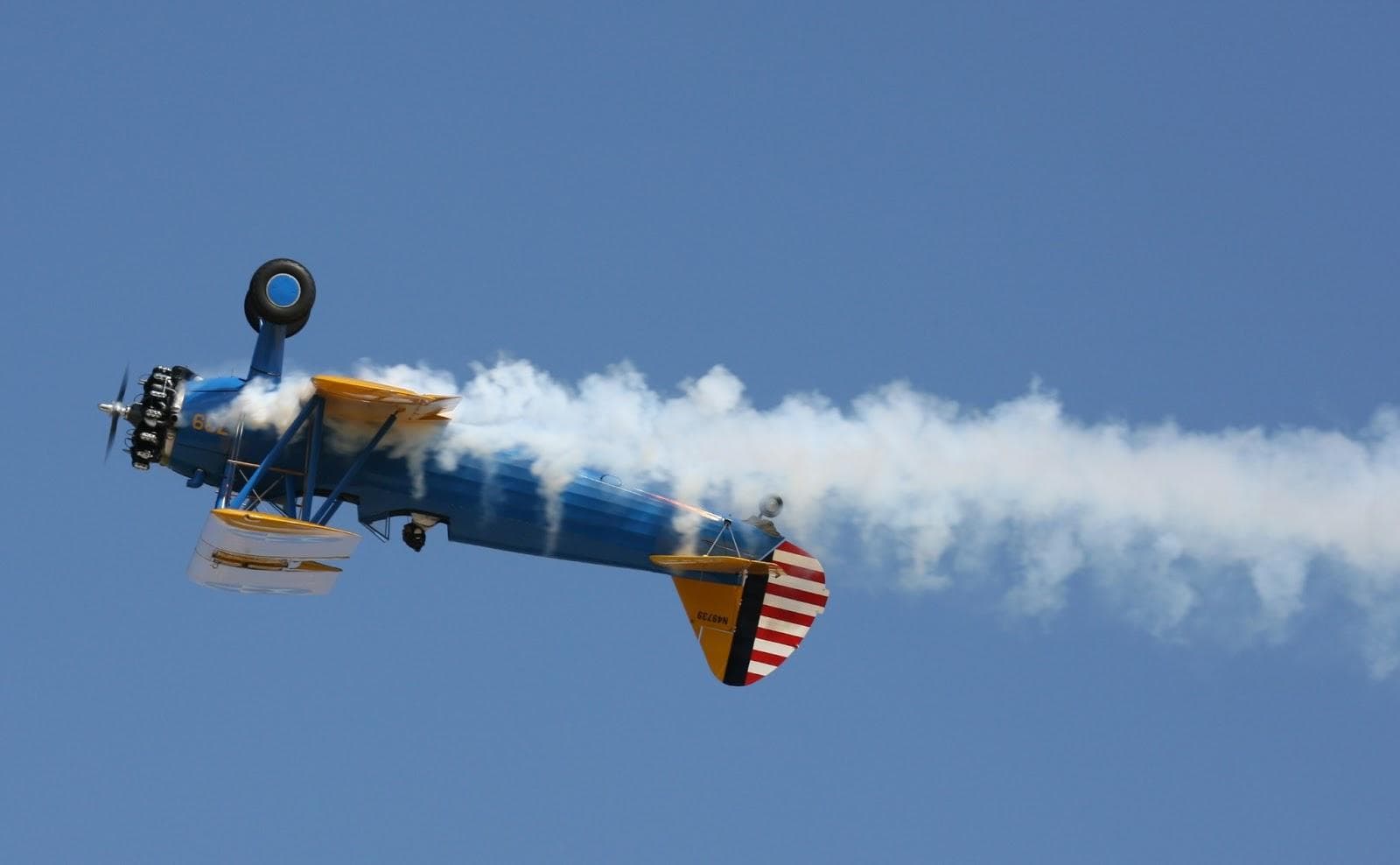 Vintage biplane performing inverted stunt trailing smoke over sky