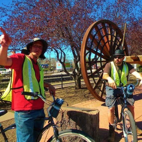 Two cyclists posing by large historic wagon wheel public art