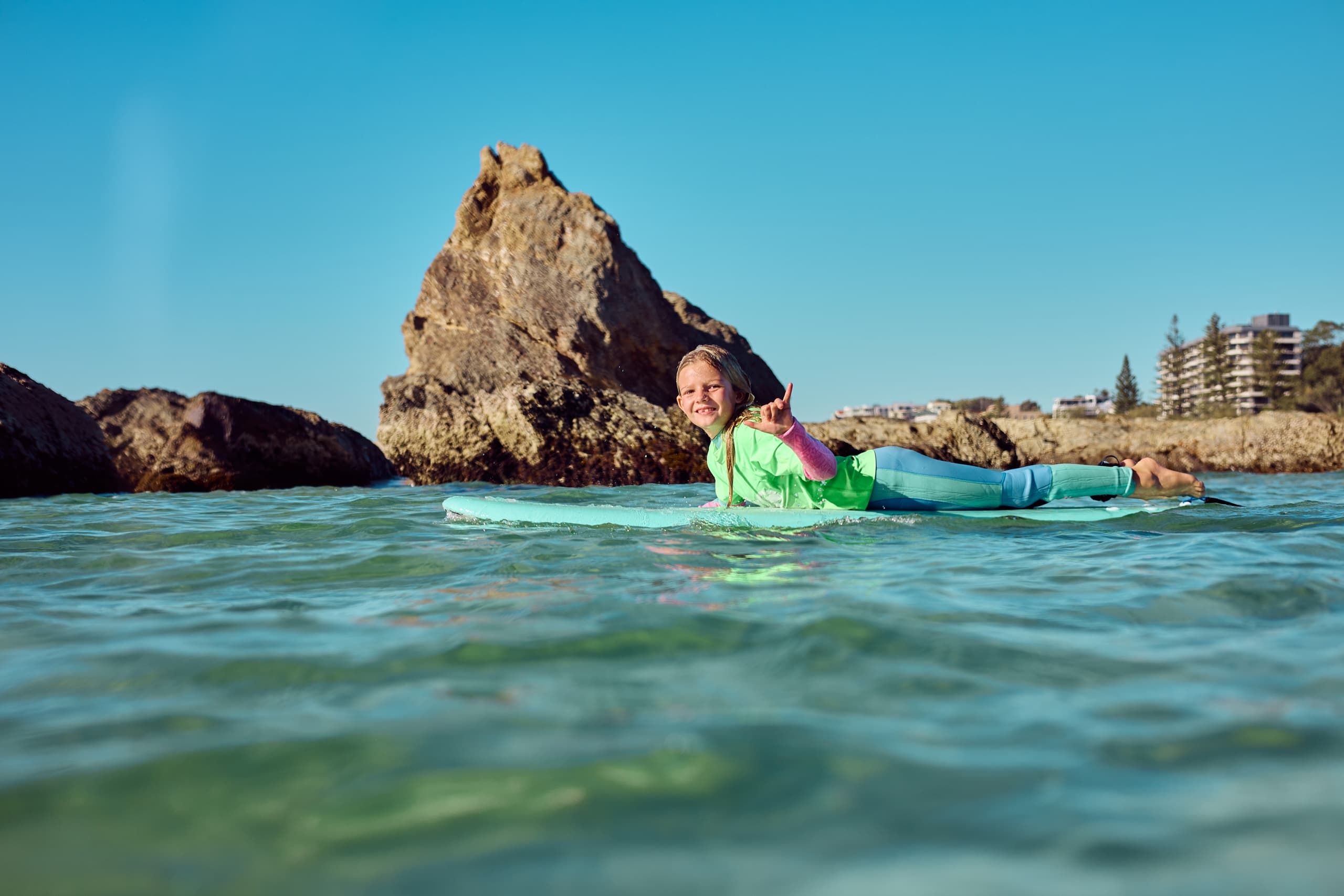 Surfer lying on board in calm ocean waters near rocky outcrop
