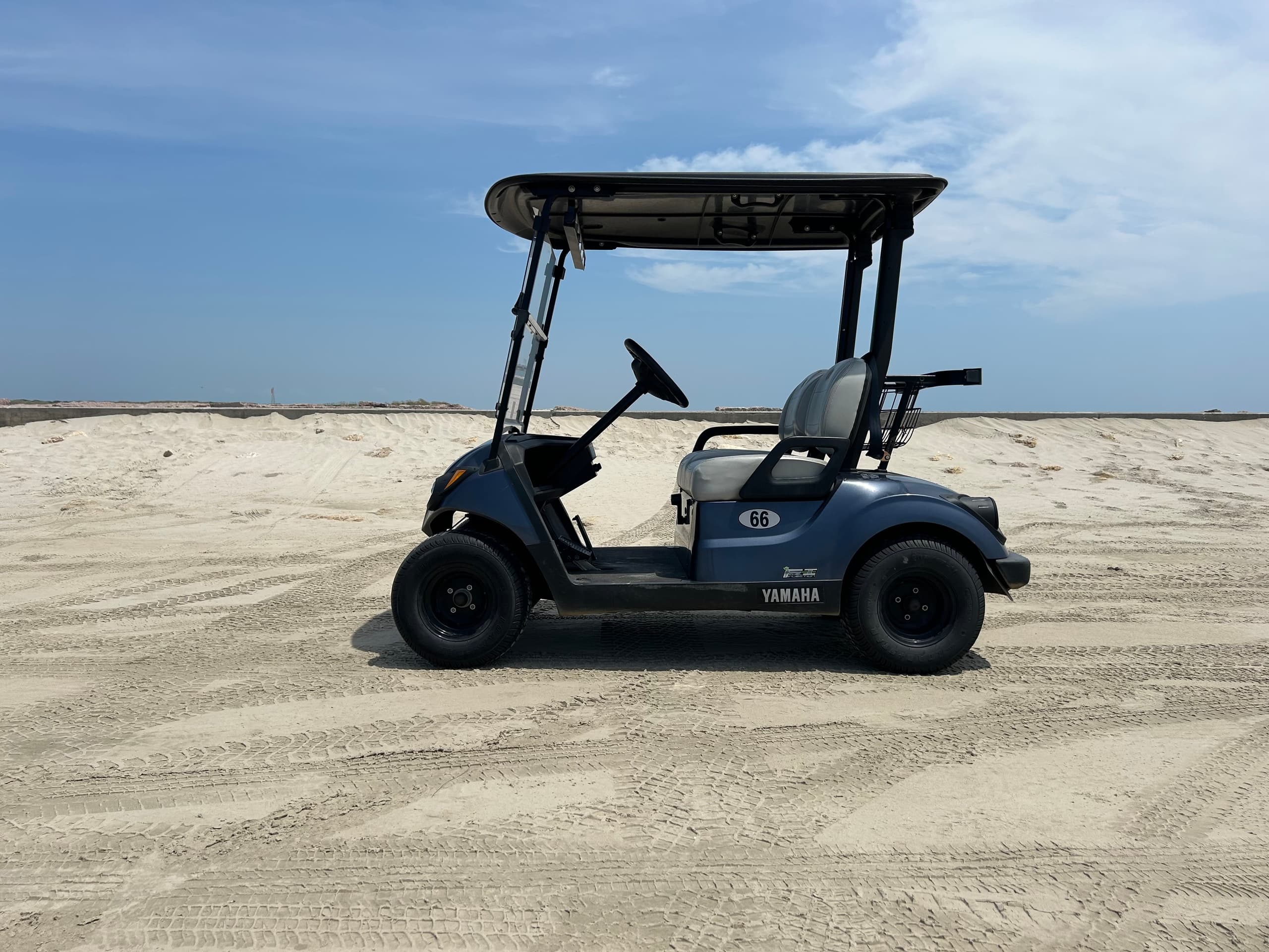 Dark blue beach golf cart parked on sandy shoreline