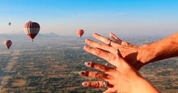 Hands reaching from hot air balloon basket over rural landscape