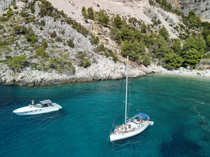 Aerial view of anchored sailboat in turquoise cove by cliffs