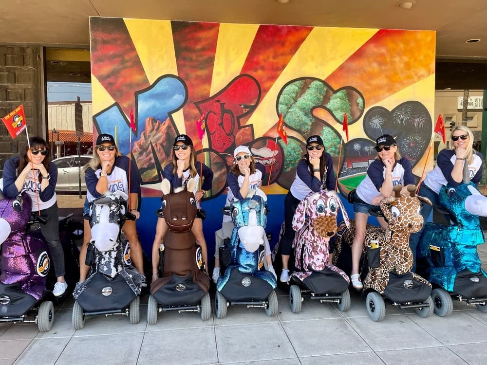 Group riding themed mobility scooters before colorful mural in Mesa