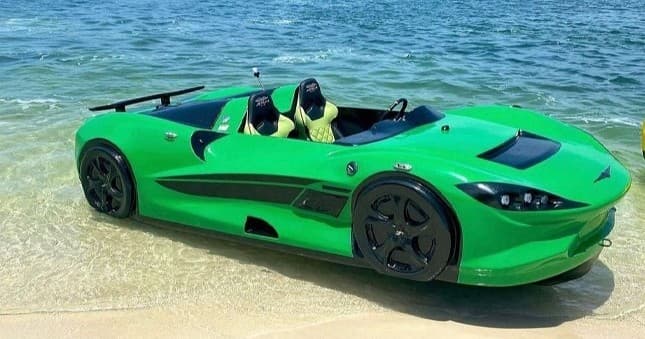 Green amphibious sports car driving in shallow ocean surf on beach