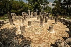 Outdoor archaeological mosaic floor with ancient columns and trees