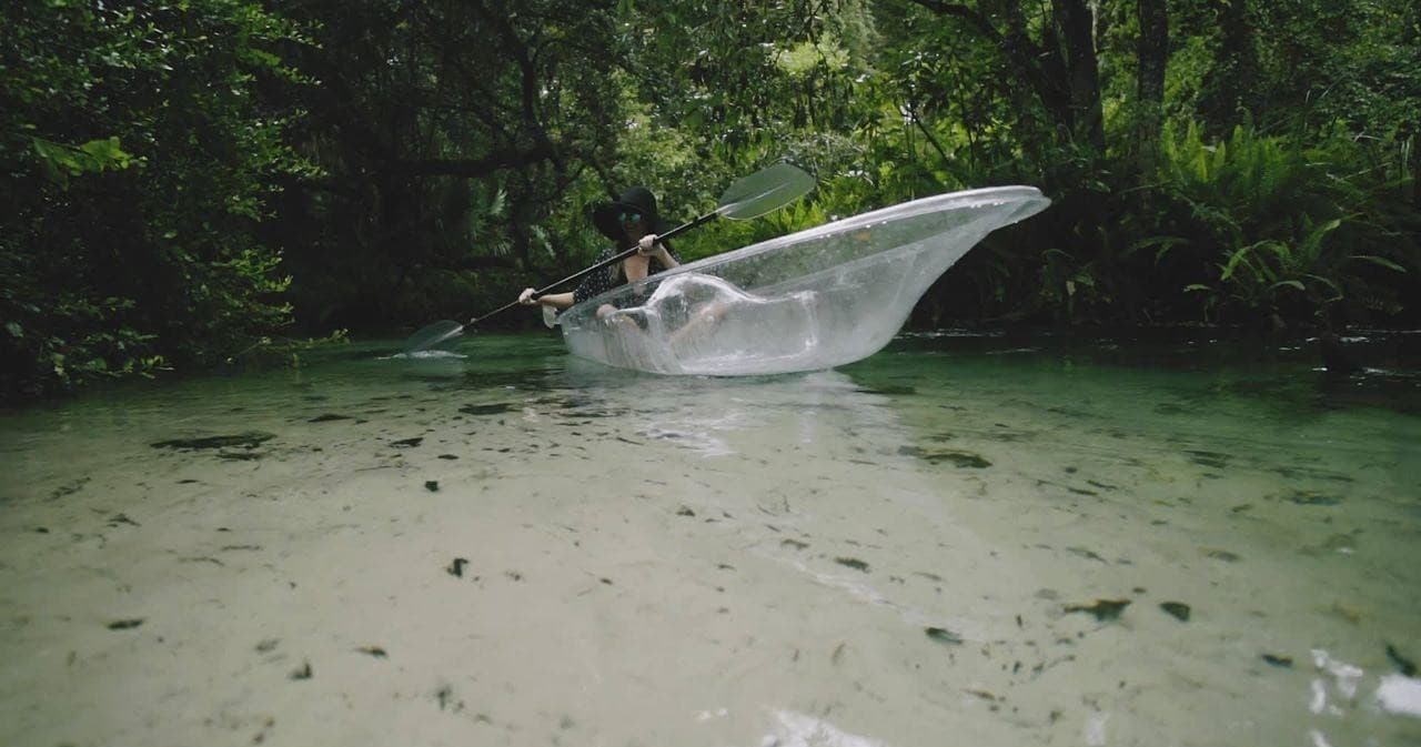 Transparent kayak skimming spring pool with paddler splashing