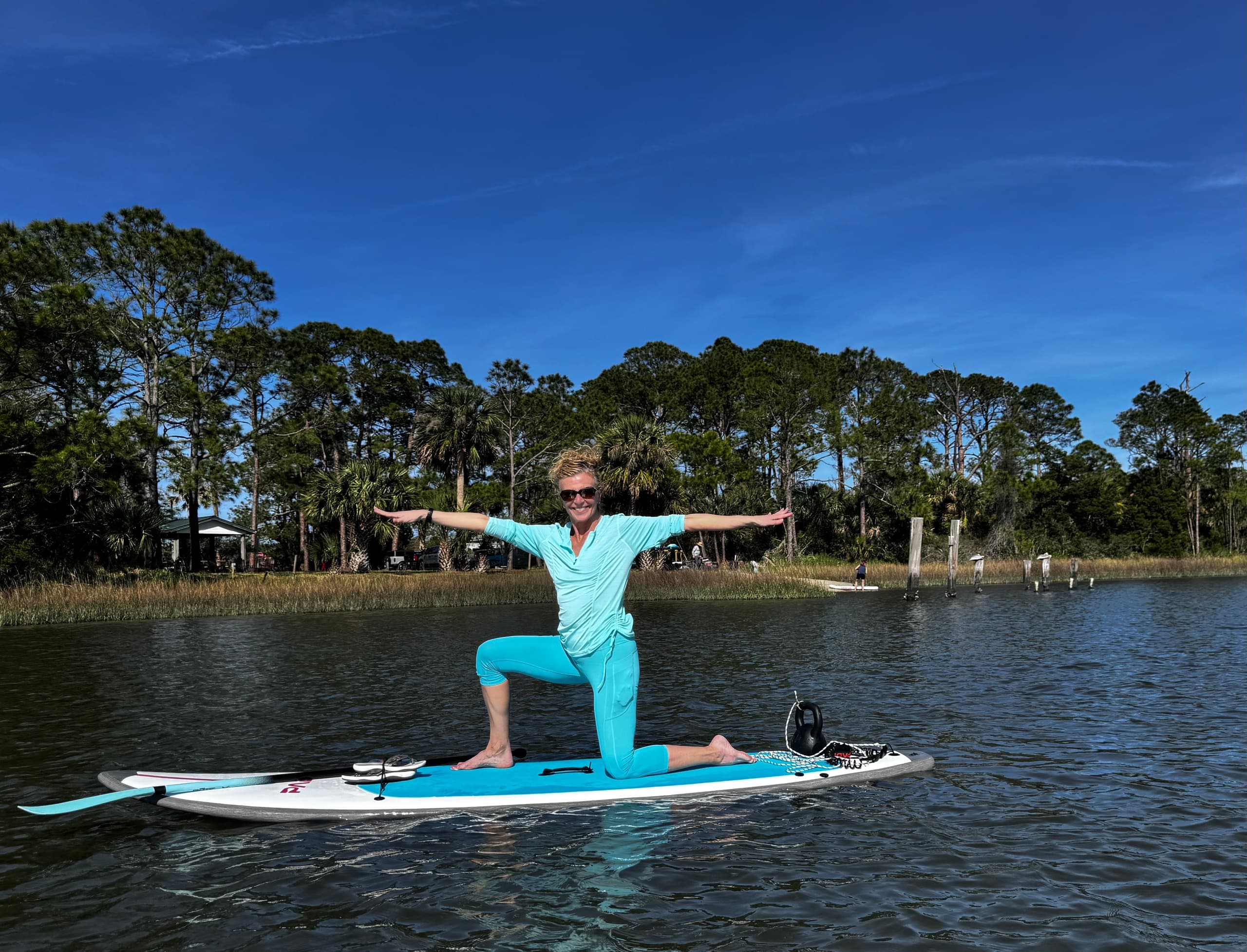 Paddleboard yoga pose on calm river beside coastal trees
