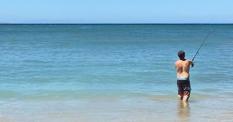 Person surf fishing waist-deep in clear Hawaiian ocean water