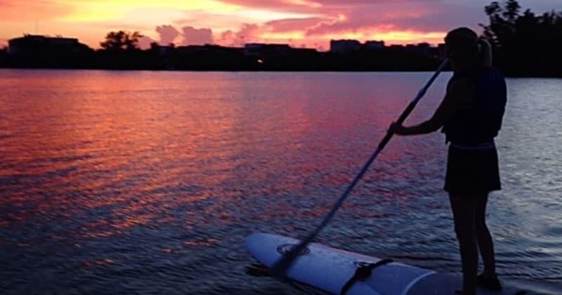 Silhouette paddleboarder at sunset over reflective estuary waters