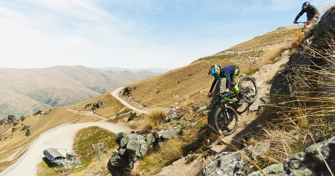Mountain biker descending rocky alpine trail with vistas NZ