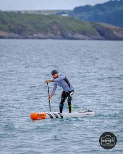 Stand-up paddler cruising coastal waters with distant cliffs
