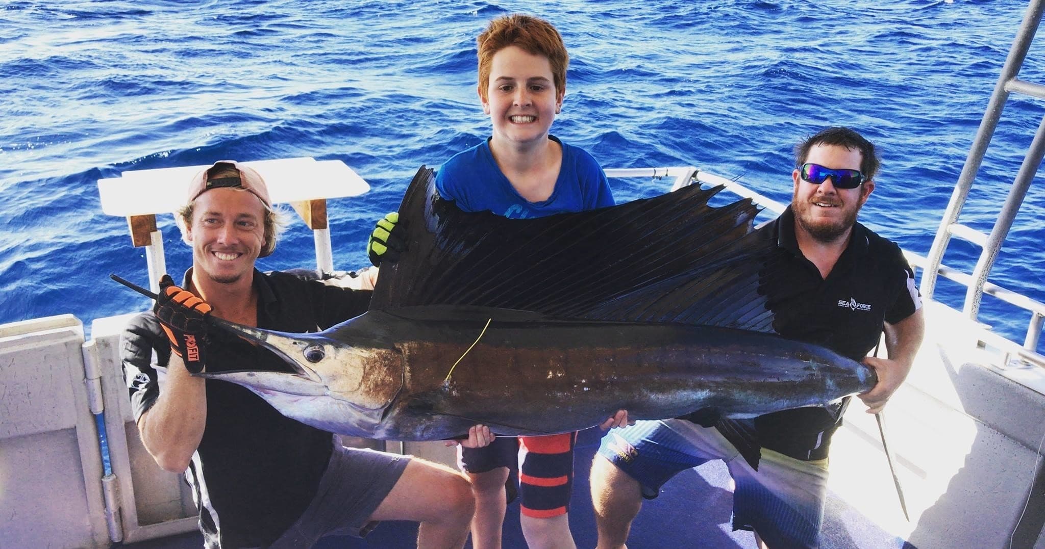Deep-sea anglers on boat holding sailfish in open ocean