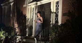 Woman standing on lit front porch at night on historic house