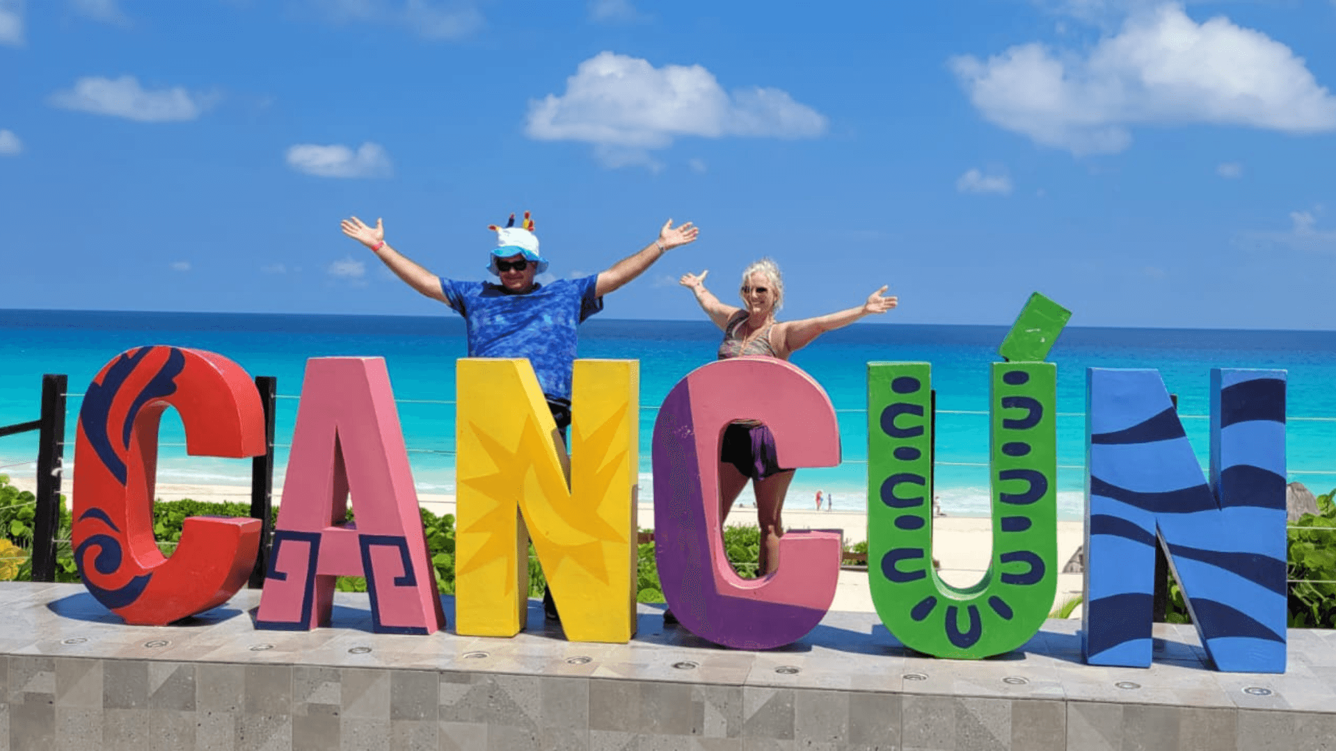 Friends at vibrant Cancun letters with ocean view and blue sky