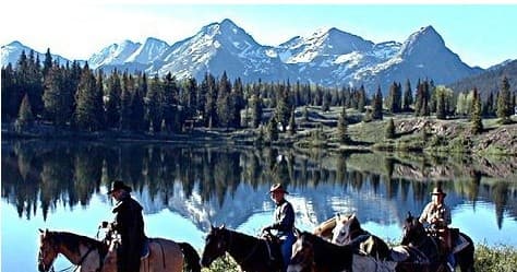 Horseback riders along alpine lake with mountain reflections