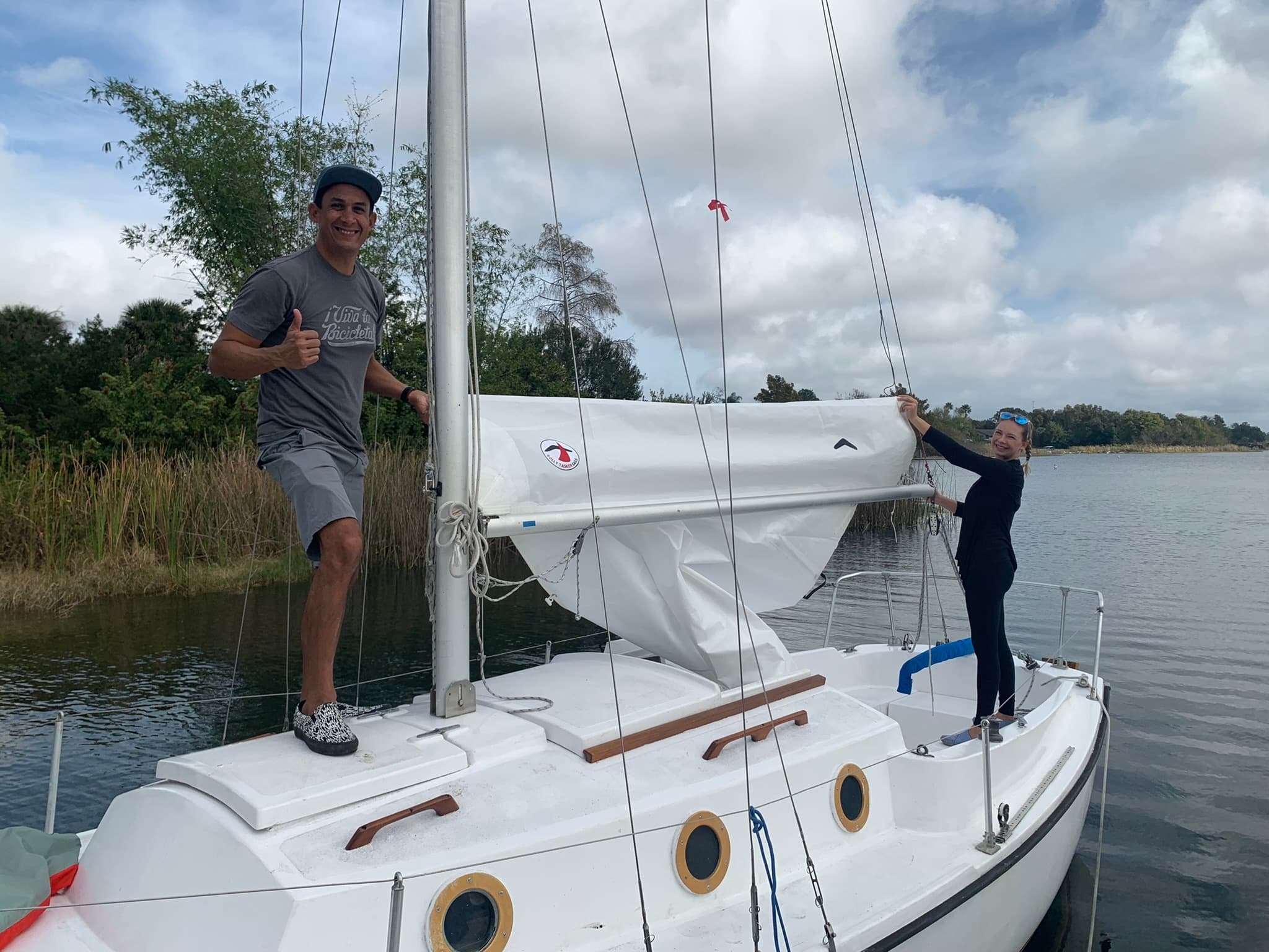 Two sailors raising sail on small cruiser in calm inland waters