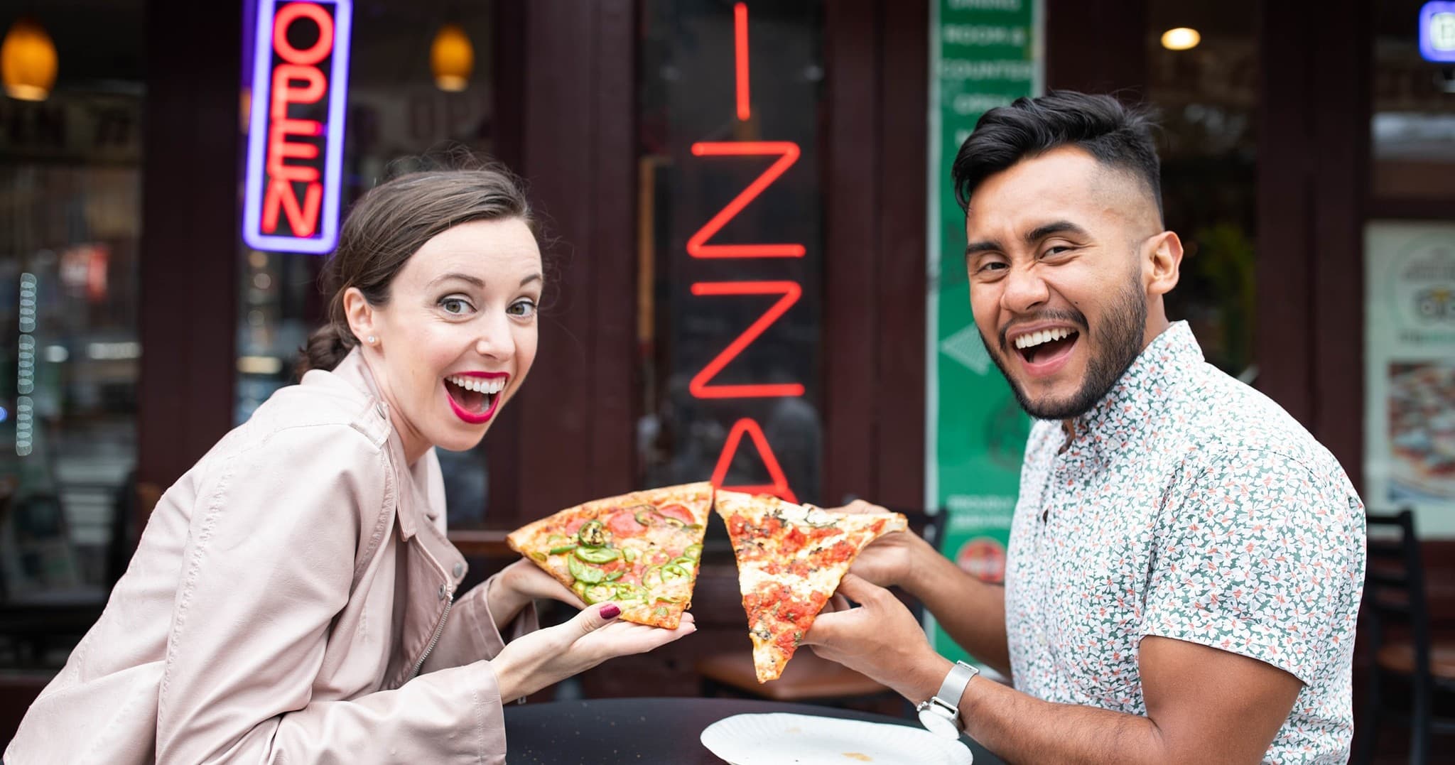 Couple sharing pizza outside a pizzeria on bustling city sidewalk