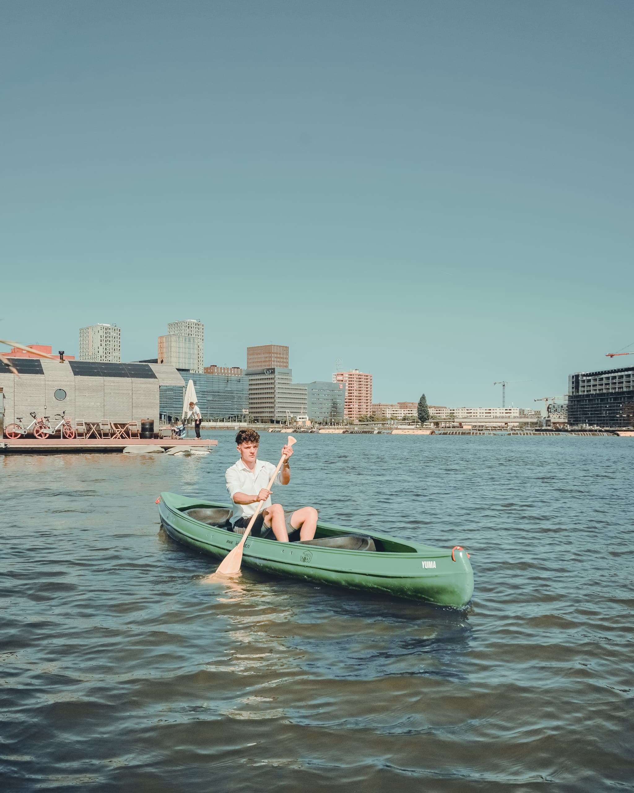 Solo paddler canoeing across city harbor with skyline backdrop