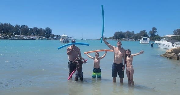 Family wading and playing in shallow turquoise bay near boats