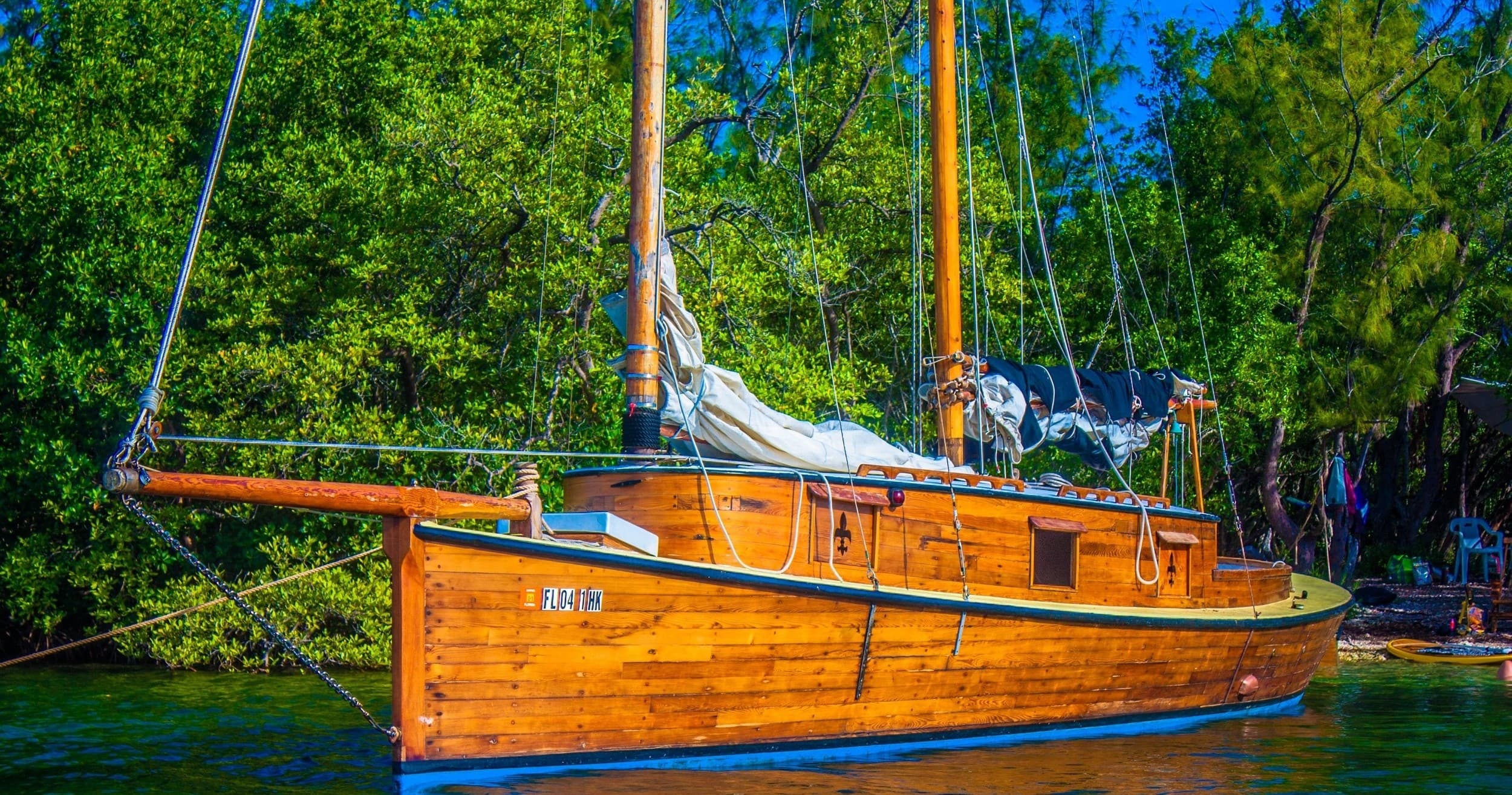 Wooden sailboat anchored near forested shore for coastal charter