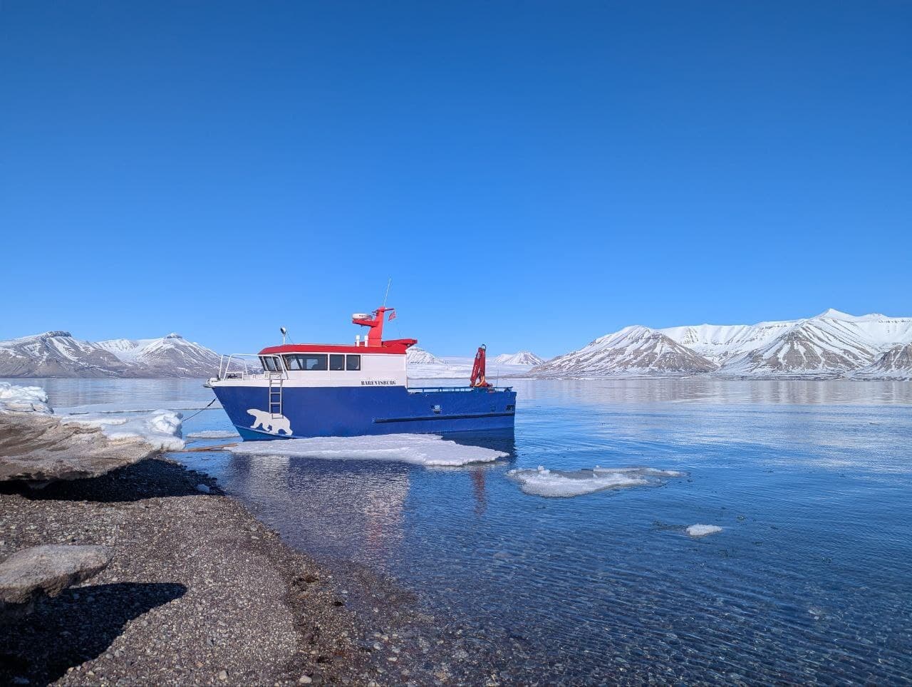 Small research ferry navigating icy fjord waters under clear sky