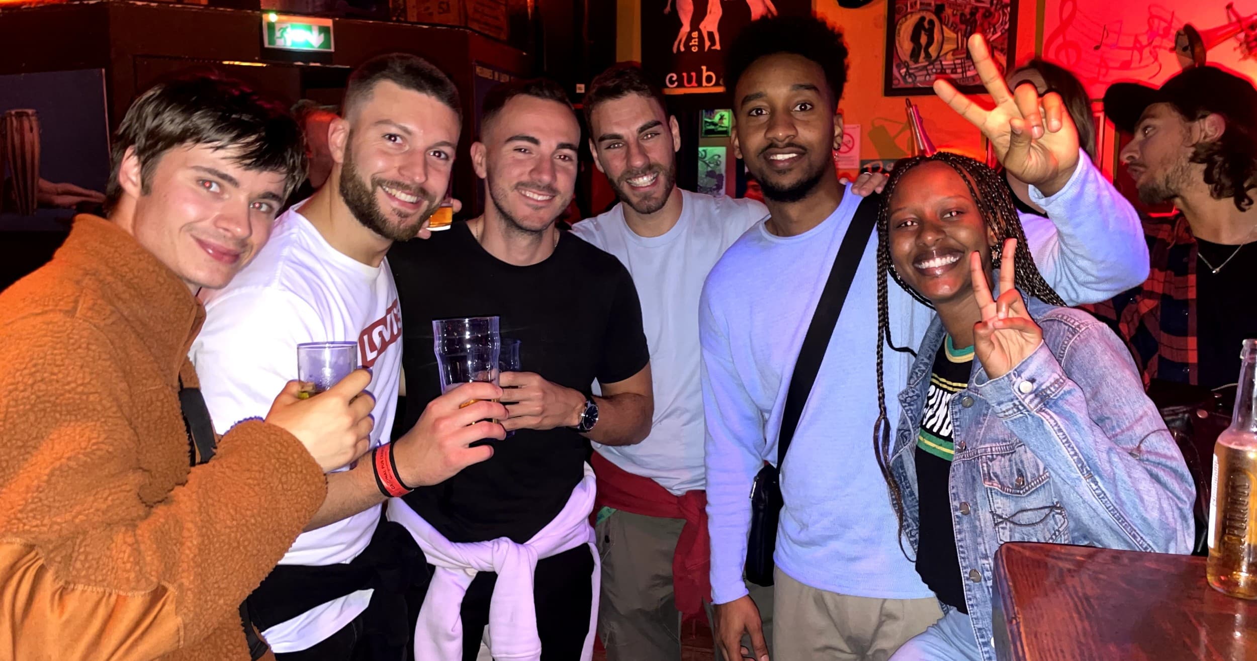 Group of friends smiling with drinks inside crowded nightclub bar