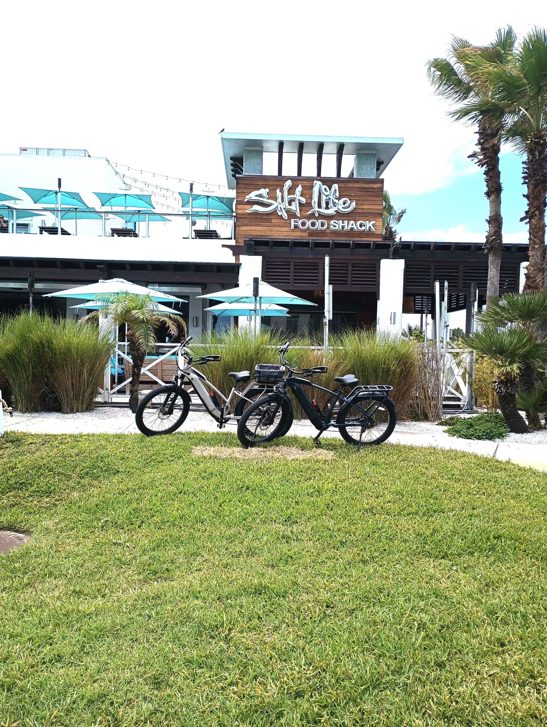 Parked rental e-bikes on grass outside beachfront food shack