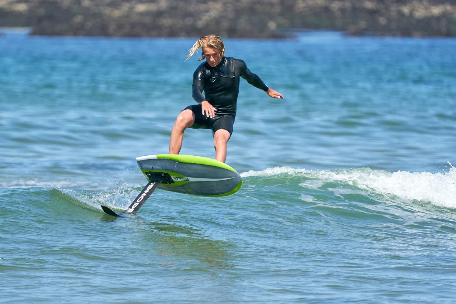 Foil surfer riding small coastal waves on clear blue sea