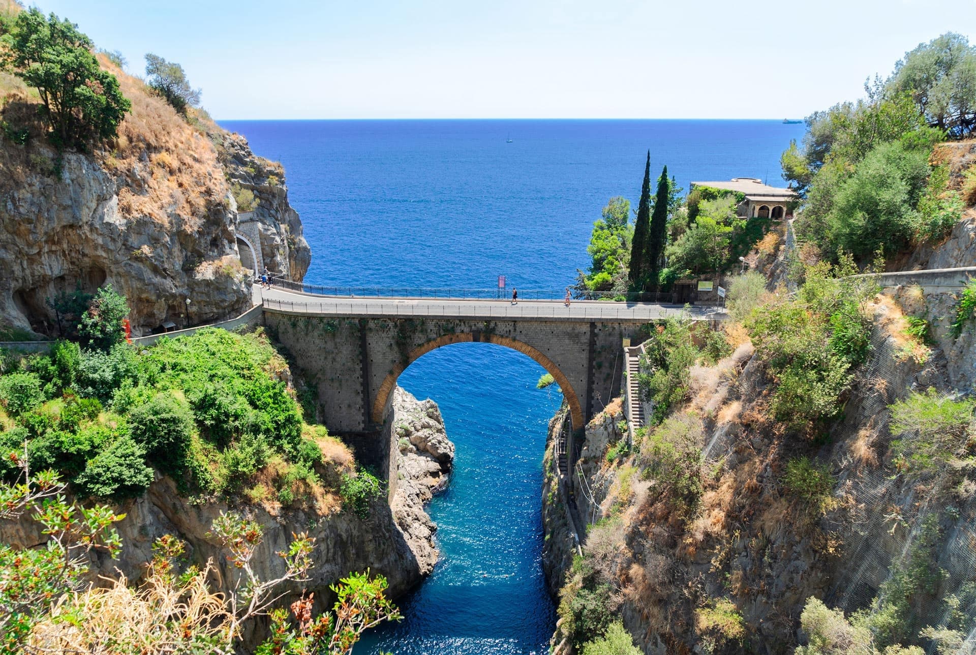 Cliffside stone bridge arch over Mediterranean inlet, ideal for scenic hikes