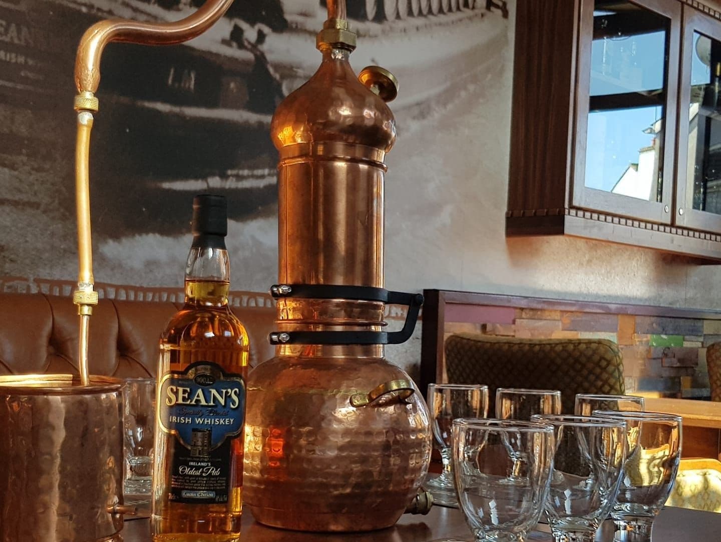 Whiskey bottle and copper still on bar counter, pub interior