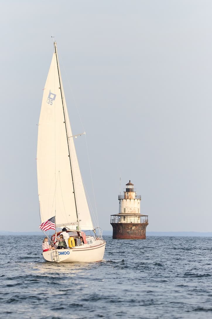 Sailboat sailing past a stone lighthouse on open coastal waters