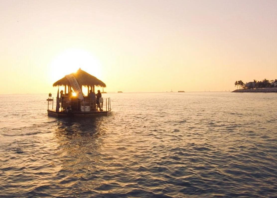 Tiki bar boat silhouetted at sunset over open ocean