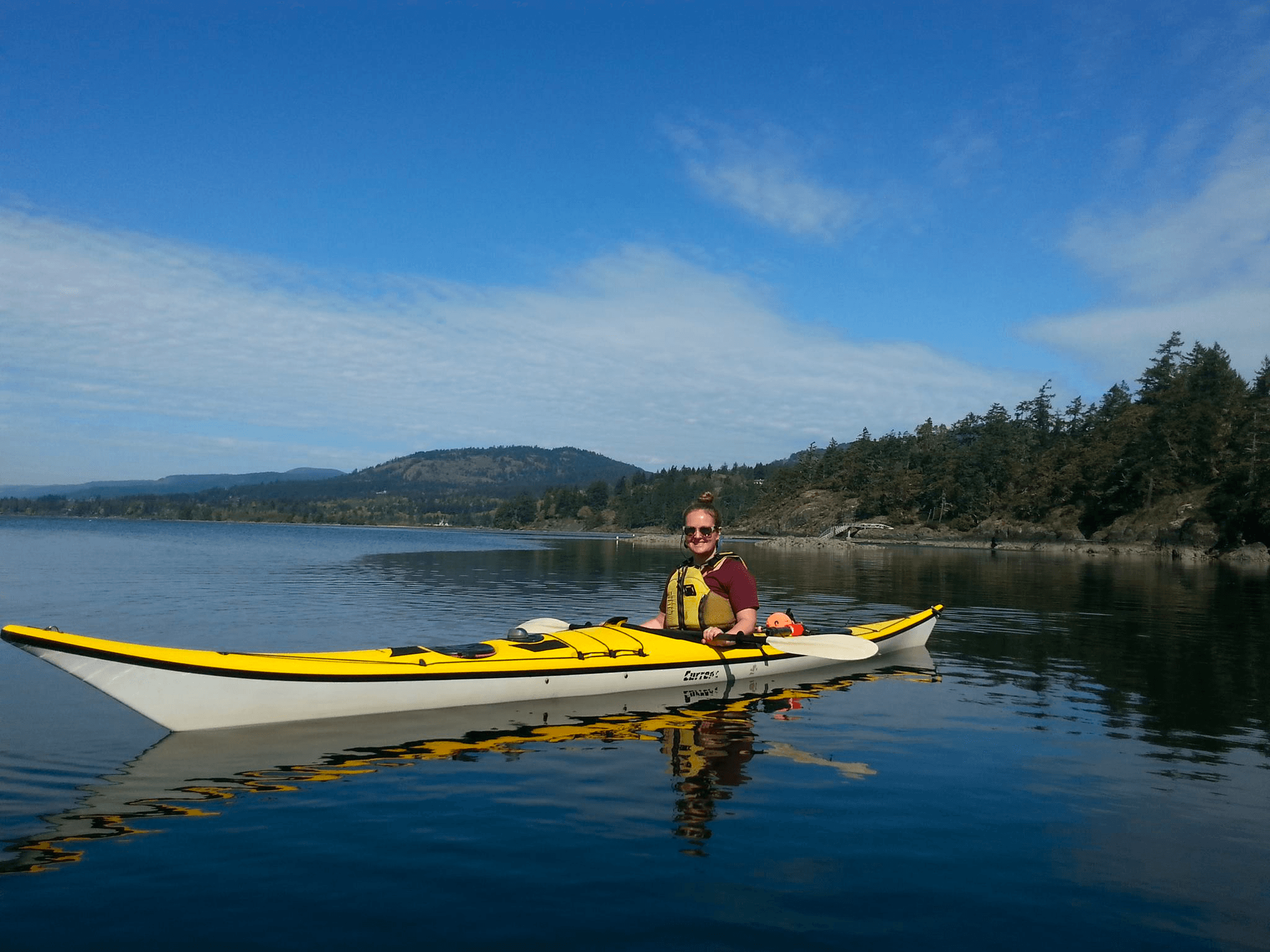 Solo kayaker paddling on calm coastal water with blue sky