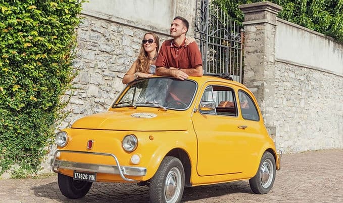 Couple driving vintage yellow Fiat on scenic Italian road trip