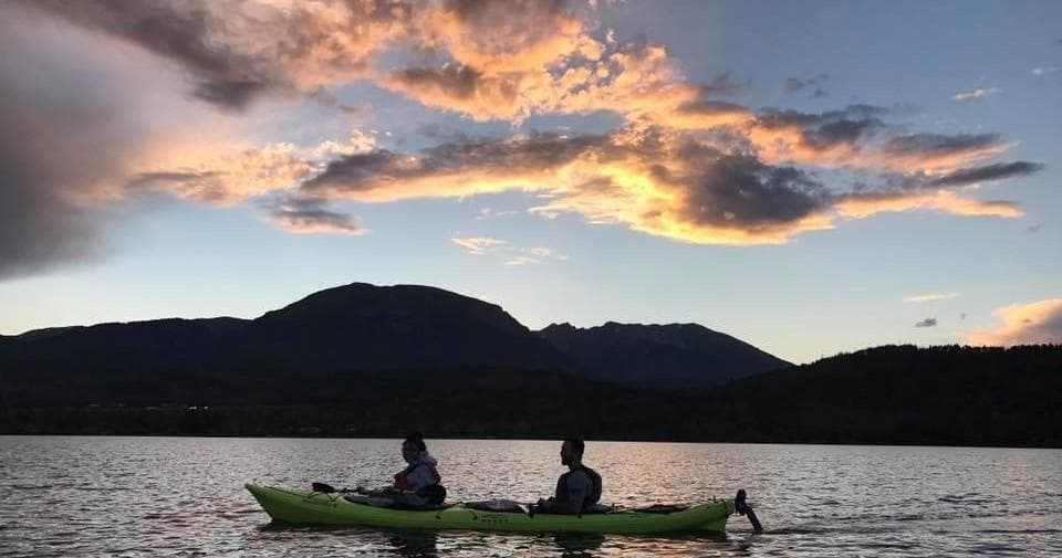 Kayakers silhouetted at sunset on alpine lake with mountains