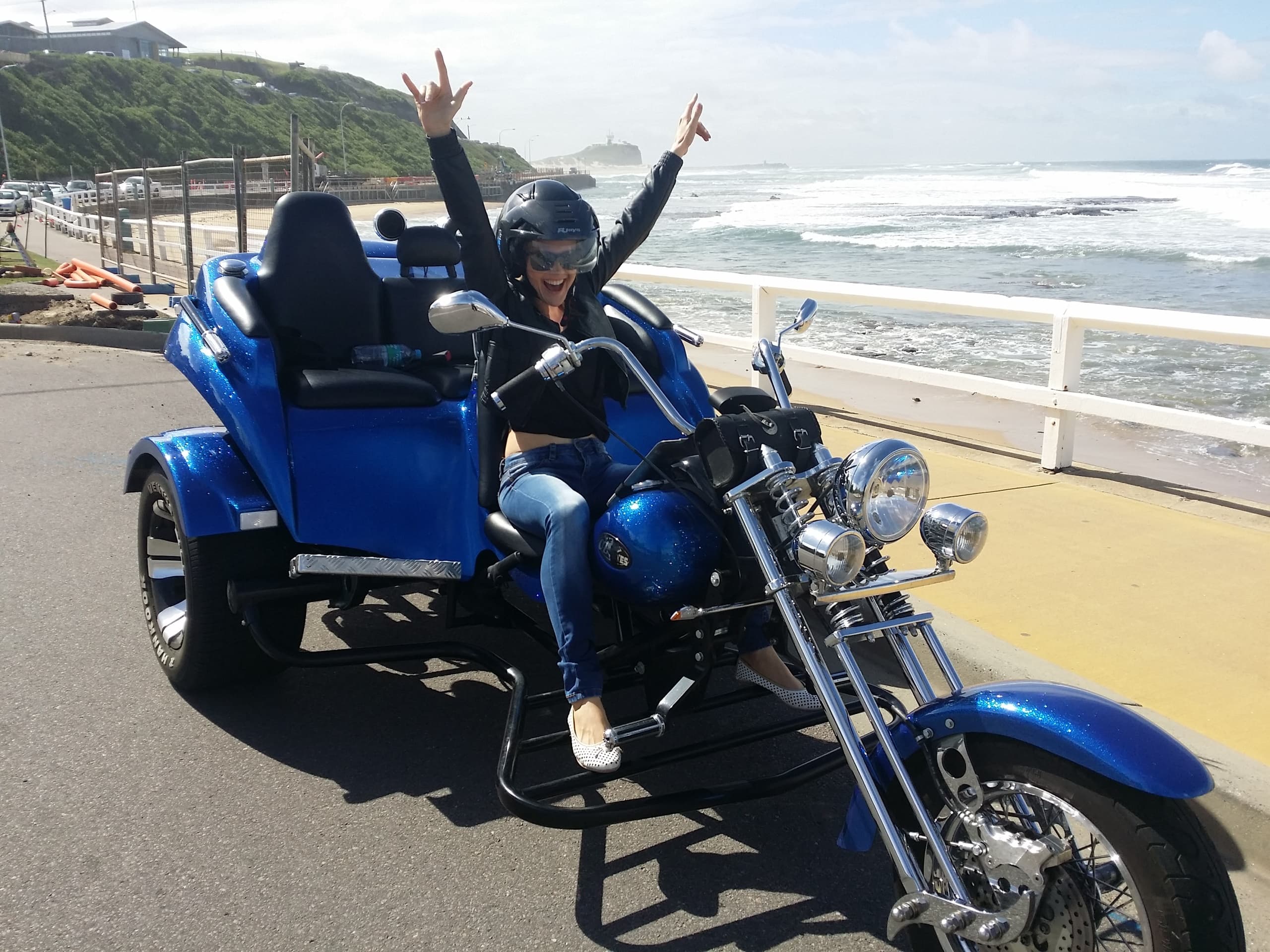Person celebrating on a blue trike by the ocean promenade enjoying ride
