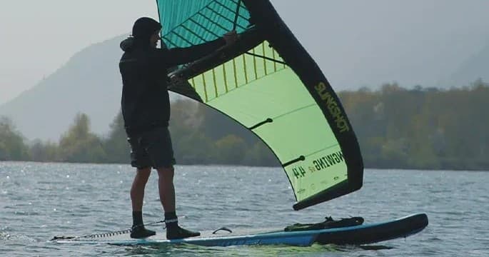 Wing foiler riding on mountain lake with distant tree-lined shore
