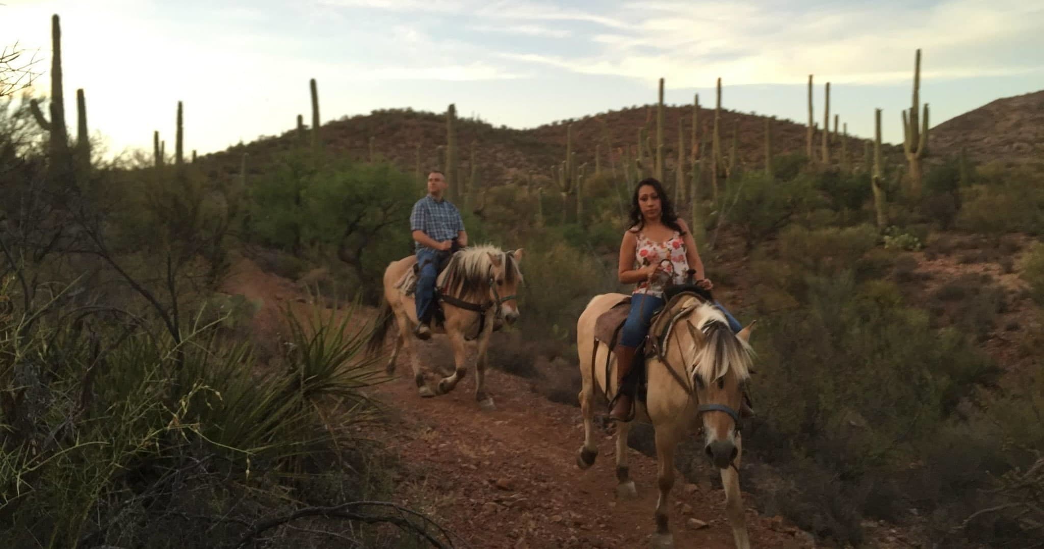 Couple horseback riding on a desert trail with saguaros