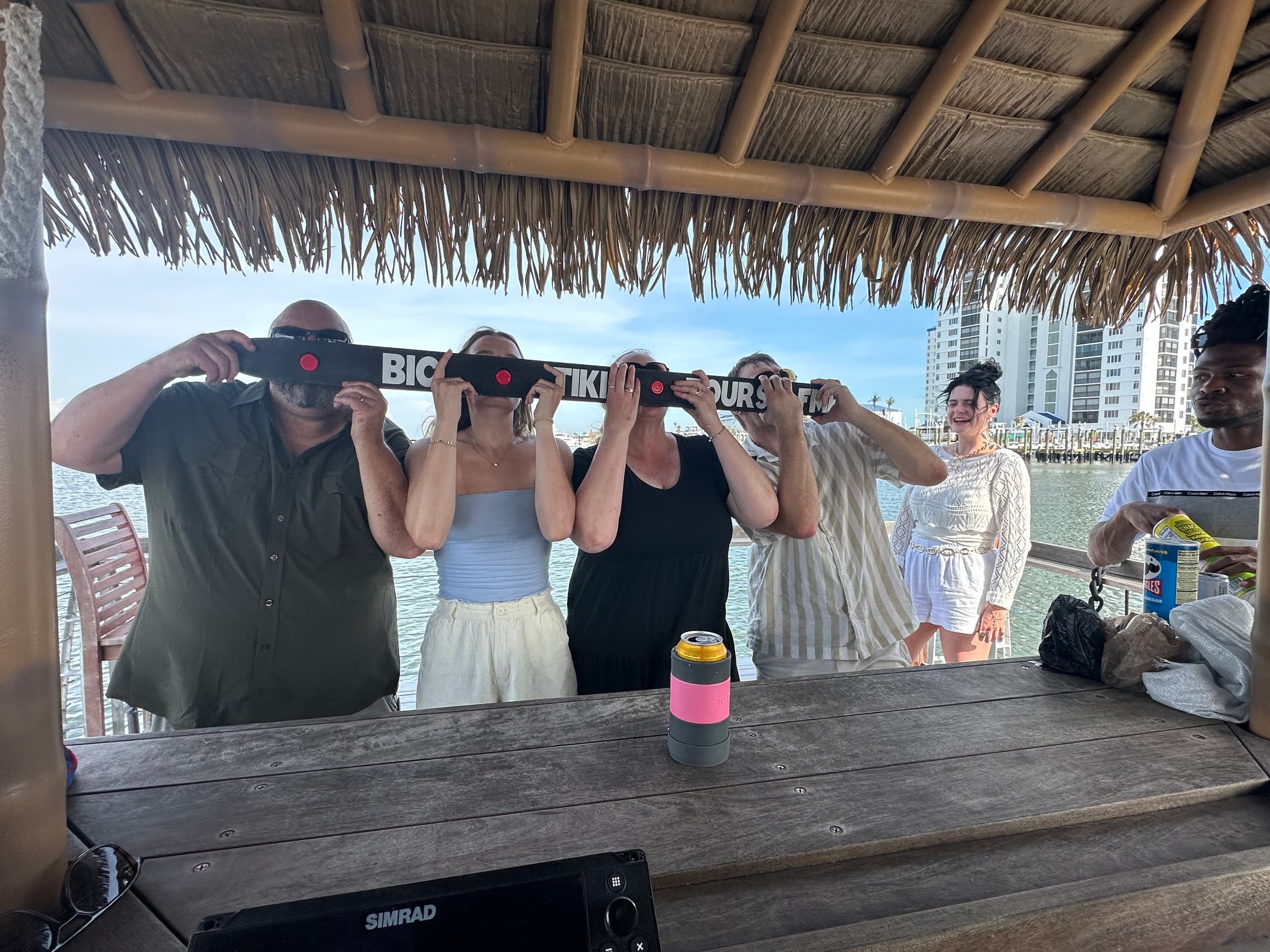 Friends sampling drinks under tiki bar aboard waterfront tour