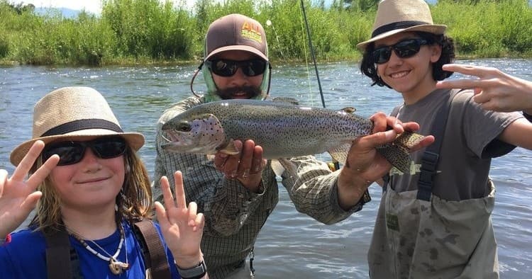 Family anglers displaying rainbow trout in sunlit river