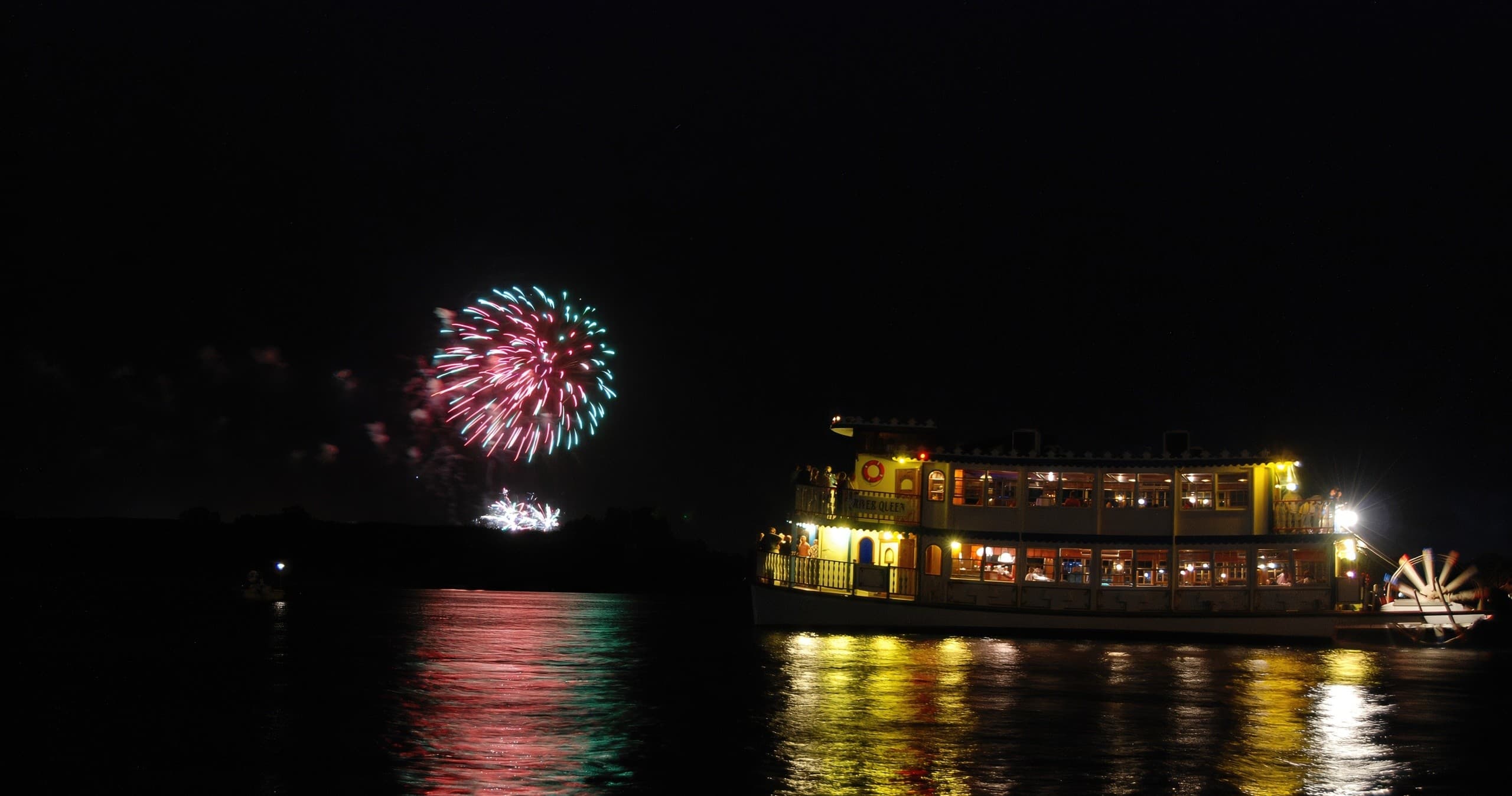 Fireworks over river with illuminated cruise boat during celebration