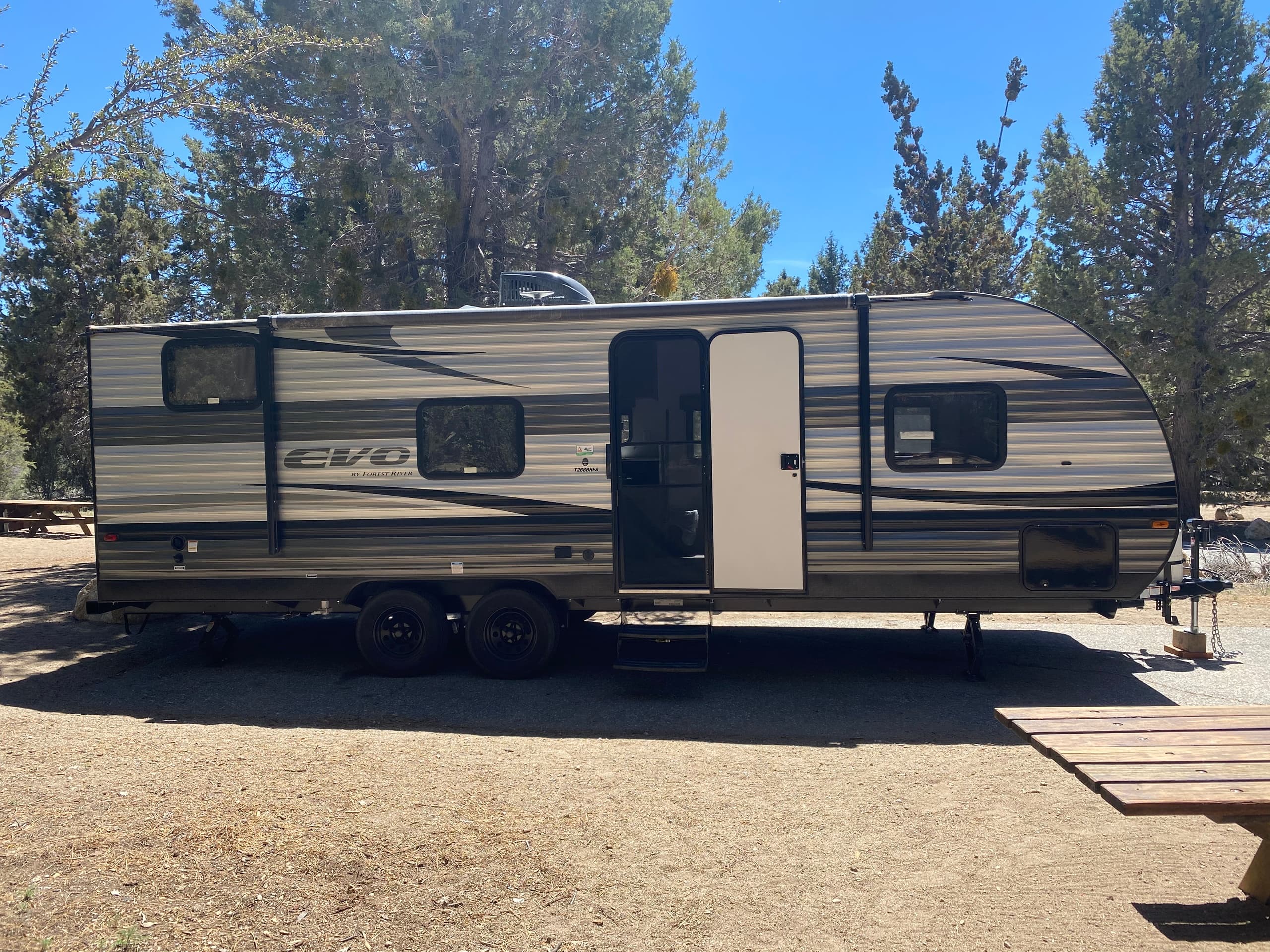Travel trailer at shaded campsite on dirt pad among trees