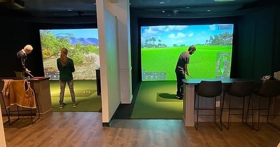 Indoor golf simulator bays with players practicing swings in studio