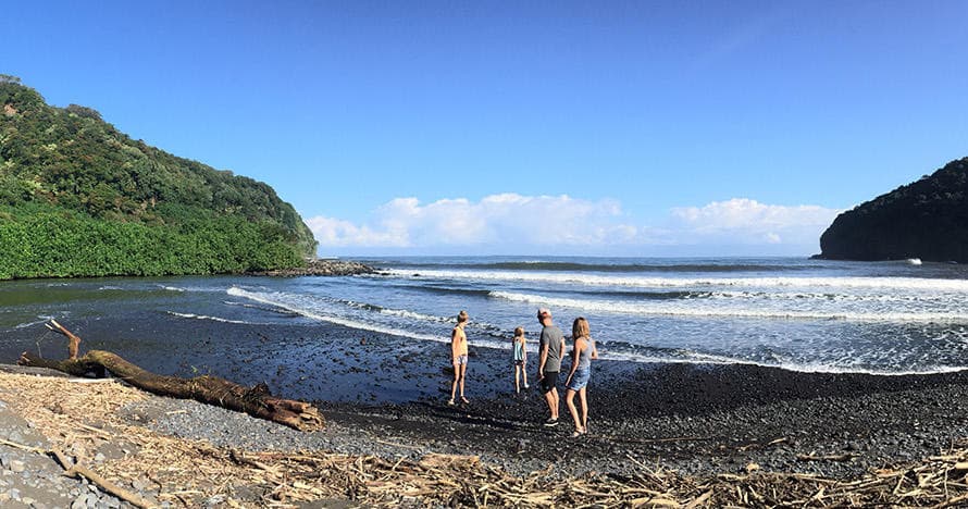 Group walking on black sand beach with ocean and cliffs