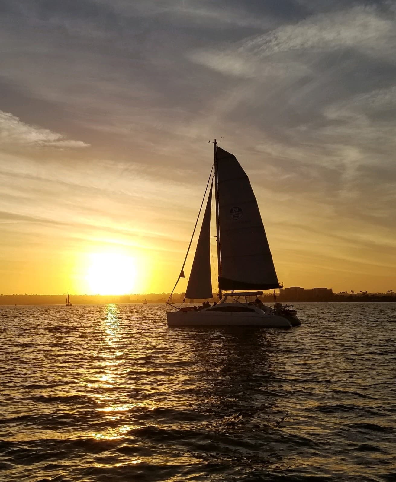 Sailing catamaran at sunset on open water with golden sky