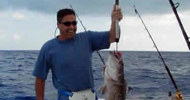 Angler displaying large fish on stern with blue ocean backdrop